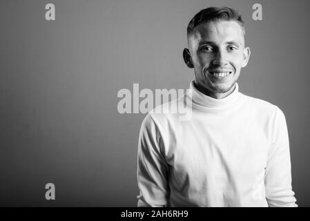 Jeune homme portant un chandail à col roulé blanc contre un fond gris Banque D'Images