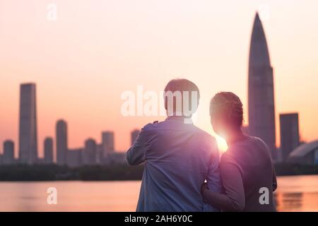 Vue arrière du senior asian couple looking at sunrise et sur les toits de la ville par la rivière Banque D'Images