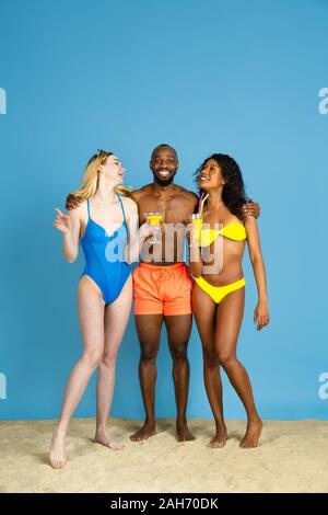 Prêts à faire la fête. Heureux les jeunes amis se reposer et s'amuser sur fond studio bleu. Concept d'émotions humaines, expression du visage, vacances d'été ou de fin de semaine. Chill, été, mer, océan. Banque D'Images