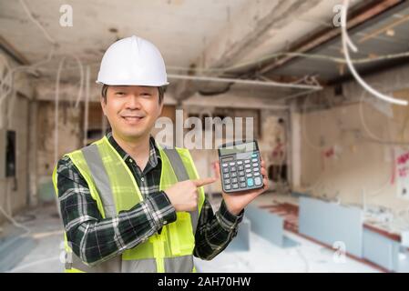 Un homme asiatique d'âge moyen portait un chapeau de travail Combinaison de travail et la tenue d'une calculatrice dans la main. Banque D'Images