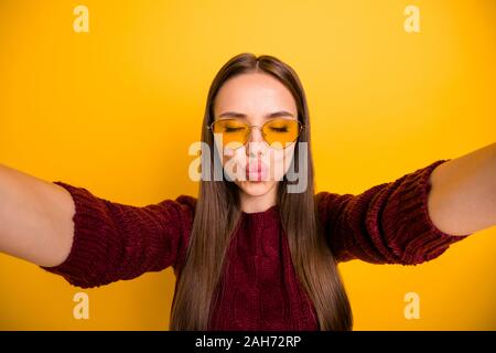 La photo en gros plan de belle fille dans l'envoi de lunettes lunettes de baisers d'air, fermant les yeux le port de pull marron sur fond jaune isolé Banque D'Images