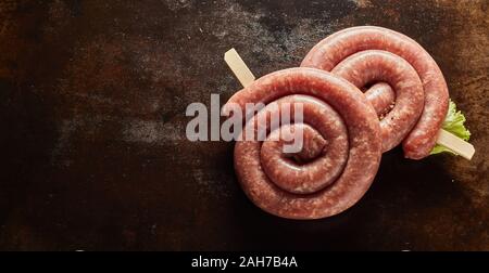 Deux bobines de saucisse crue épicée dans un panorama banner sur une plaque de métal sombre contexte placé sur le côté avec copie espace pour la publicité Banque D'Images