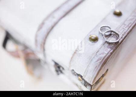 Deux anneaux de mariage blancs en or couchés sur un blanc abîmé poitrine en bois sur fond bokeh Banque D'Images