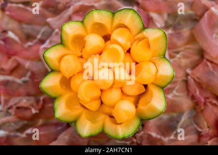 Gros plan symétrique d'un melon tranché sur un plateau de jambon, tiré par le dessus Banque D'Images