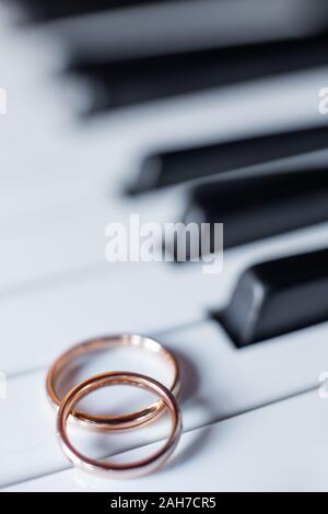 Gros plan de deux anneaux de mariage dorés reposant sur un grandes touches de piano Banque D'Images