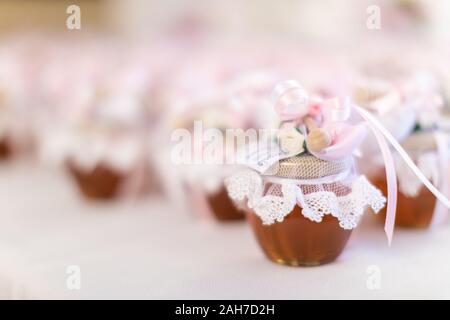 Gros plan d'un certain nombre de faveurs de mariage, sous forme de pots de miel décorés de dentelle blanche et de rubans roses, sur fond de bokeh Banque D'Images