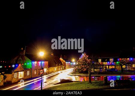 Les sentiers de la lumière des véhicules de passage vu le long d'une rue de village humide reflétant les lumières de Noël dans le village de Sharnbrook Bedfordshire Banque D'Images