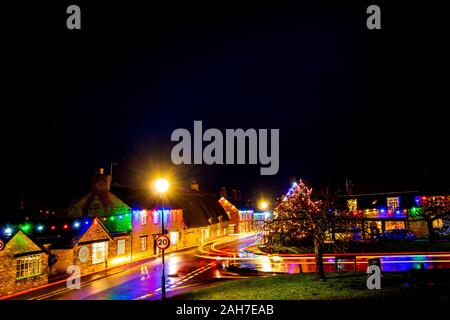 Les sentiers de la lumière des véhicules de passage vu le long d'une rue de village humide reflétant les lumières de Noël dans le village de Sharnbrook Bedfordshire Banque D'Images