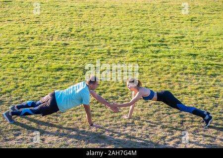 Jeune couple de mettre en place les sportifs boy and girl doing exercise sur l'herbe verte de l'extérieur du stade. Banque D'Images