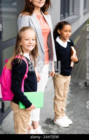 Portrait de mère tenant les mains de deux filles en uniforme de l'école multiculturelle Banque D'Images