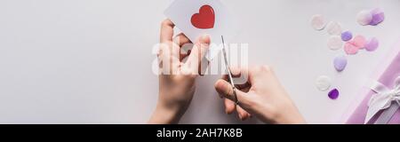 Portrait de femme se coupe avec des ciseaux coeur cadeau saint valentin proche sur fond blanc, vue panoramique tourné Banque D'Images