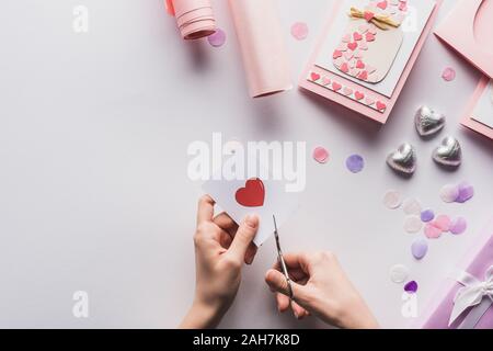 Portrait de femme se coupe avec des ciseaux coeur près de décoration, Cadeaux saint valentin, coeurs et papier d'emballage sur fond blanc Banque D'Images