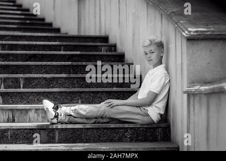 Portrait monochrome (noir et blanc) de joli beau blond onze vieux garçon (adolescent) assis sur les escaliers extérieur.Grandir, puérile, séparation Banque D'Images