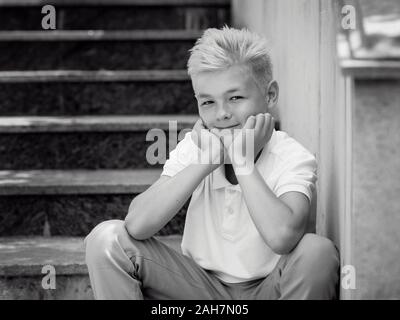 Portrait monochrome (noir et blanc) de joli beau blond onze vieux garçon (adolescent) assis sur les escaliers extérieur.Grandir, puérile, séparation Banque D'Images