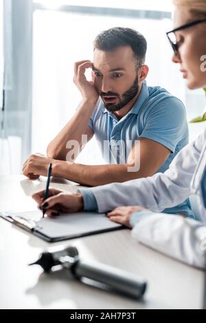 Portrait d'homme barbu choqué à la médecin au diagnostic d'écriture Banque D'Images