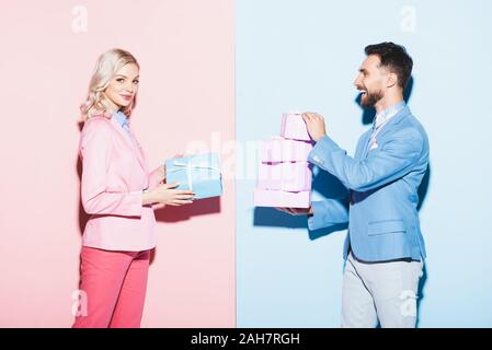 Jolie femme et smiling man holding gifts sur fond bleu et rose Banque D'Images