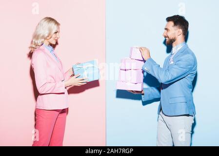 Vue de côté de femme séduisante et smiling man holding gifts sur fond bleu et rose Banque D'Images