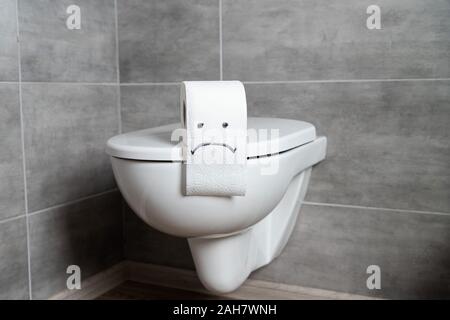 Le papier de toilette avec emoticon triste sur la cuvette des toilettes dans salle de bain moderne Banque D'Images