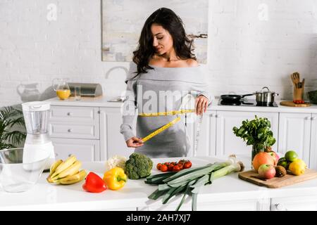 Attractive Woman measuring waist près de fruits et légumes sur le tableau Banque D'Images