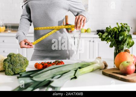 Portrait of woman measuring waist près de légumes sur la table Banque D'Images