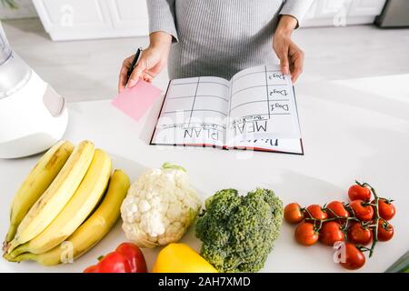 Portrait de femme près de l'ordinateur portable avec des repas et des légumes sur la table Banque D'Images