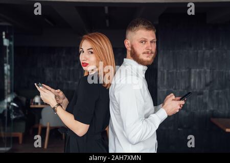 Les jeunes se tenir avec le dos à l'autre avec un smartphones dans les mains. Banque D'Images