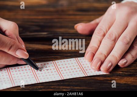 Portrait de joueur marquant les chiffres en billet de loterie avec un stylo sur la table en bois Banque D'Images