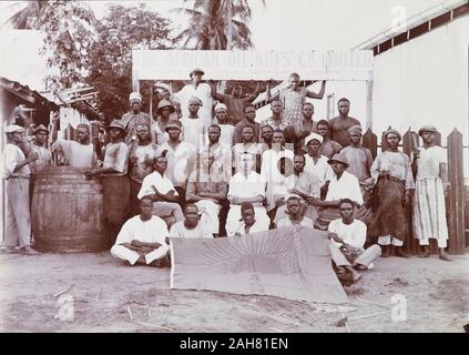 Le Nigéria, portrait de groupe d'un superviseur européen et africain du personnel de la Société africaine à l'huile de noix assis sous le signe de l'entreprise qui se lit comme suit : "l'huile de noix africaine Co. Limited, Maison Centrale, Kingsway, London". Bon nombre des gardiennes d'effectuer les outils de leur métier, plusieurs actions mimant avec eux. Les cinq hommes à l'avant-plan afficher un grand drapeau, qui montre le soleil levant et les lettres 'AON'. Marquage sur la marche arrière : 'A. O. N. Personnel, Badagry, mai 1922". , Mai 1922. 2/26/2000/098. Banque D'Images