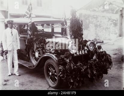 Le Nigeria, le marquage au verso : Jour du Souvenir.Un chauffeur stands africains, à côté d'une voiture décorée de feuillage et drapeaux de l'Union européenne à l'occasion du Jour du Souvenir, [c.1920s]. 2/79/2000/098. Banque D'Images