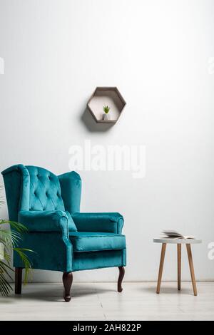 Intérieur de prix avec un élégant fauteuil velour blue près de plante verte et table à café près de mur blanc Banque D'Images