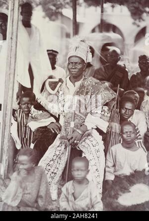 Le Nigeria, le marquage au verso : '1927 Badagry'Un chef non identifié, peut-être l'Akran de Badagry, est assis portant des robes brodées avec un haut-verso et les pampilles. Il est titulaire d'un personnel de bureau et est entouré par des enfants assis sur le sol, l'un d'entre eux est titulaire d'un ventilateur bordés de plumes, 1927. 2/97/2000/098. Banque D'Images