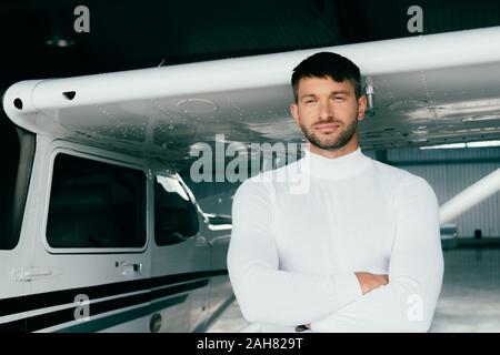 Beau jeune homme en tenue décontractée debout les bras croisés, près de avion Banque D'Images