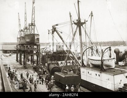 Au Kenya, en vue de dessus de la grue à bord de SS Harmonides la descente d'une chaudière de locomotive sur la voie ferrée à quai au port de Kilindini, si une offre est déjà. Ouvriers sont debout à proximité. Partie d'une série montrant la locomotive le déchargement, [1920]. 1999/135/1/1/4. Banque D'Images