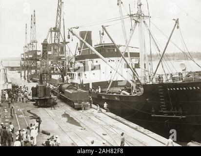 Au Kenya, une chaudière de locomotive et l'offre ont été abaissé sur un bogie sur le quai du port de Kilindini à chemin de fer par des grues à bord de SS Harmonides. Une grue à vapeur se distingue par le train. Ouvriers sont debout à proximité. Partie d'une série montrant la locomotive le déchargement, [1920]. 1999/135/1/1/1. Banque D'Images