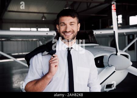 Smiling pilote en tenue de cérémonie, debout près de l'avion et looking at camera Banque D'Images