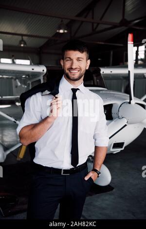 Smiling pilote en tenue de cérémonie, debout près de l'avion et looking at camera Banque D'Images