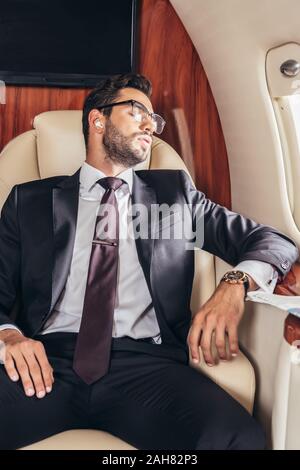 Handsome businessman in suit le sommeil et l'écoute la musique en avion privé Banque D'Images