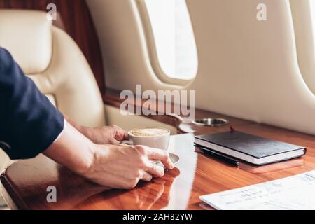 Portrait de l'agent de bord mettant tasse de café sur la table en avion privé Banque D'Images