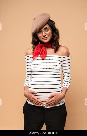 Femme enceinte en français béret looking at camera sur fond beige Banque D'Images