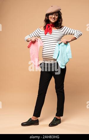 Femme enceinte en français béret holding bretelles sur fond beige Banque D'Images