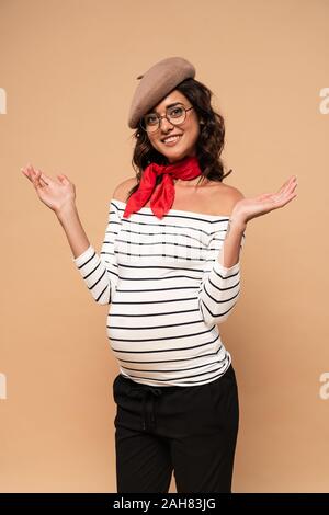 Femme enceinte en français béret tendre la main en souriant sur fond beige Banque D'Images