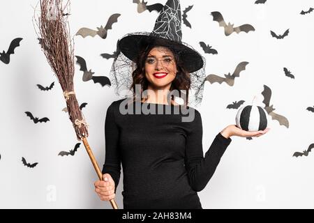 Femme enceinte au chapeau de sorcière holding broom et citrouille à l'Halloween Banque D'Images