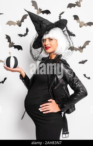 Femme enceinte en perruque et chapeau de sorcière Halloween citrouille dans holding Banque D'Images