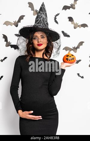 Femme enceinte au chapeau de sorcière Halloween citrouille dans holding Banque D'Images