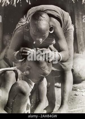 Au Kenya, une mère Kikuyu se penche sur de sa fille pou de tête rasée. Manuscrit original légende : De-lousing enfants fait partie d'une des fonctions de la mère. S. 1936, 1937 de Nyeri. 1995/076/1/2/5/14. Banque D'Images