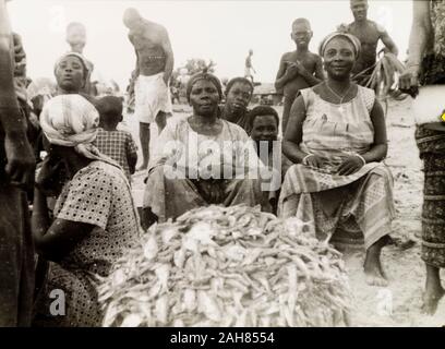 CoastGhana d'or, les commerçantes s'asseoir à côté d'un tas de poissons fraîchement pêchés at a market stall à Elmina. Manuscrit original description : mammies marché acheter le poisson à Elmina, 1951-1952. 1995/076/5/2/2/55. Banque D'Images