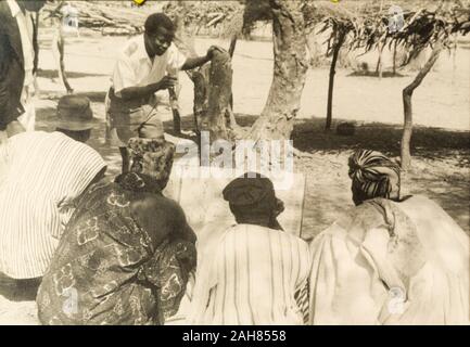 CoastGhana Gold, un étudiant enseignant aide les hommes à lire à partir d'une sélection au cours d'une classe d'alphabétisation ; partie d'une campagne d'alphabétisation de masse lancée par le gouvernement britannique en 1951 pour améliorer les aptitudes en littératie chez les adultes, tant dans leur propre langue et en anglais. Manuscrit original légende : élève-maître d'une classe d'alphabétisation de masse en NTs [Territoires du Nord], 1951-1952. 1995/076/5/2/2/44. Banque D'Images