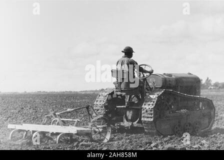 Au Kenya, une main ferme africaine utilise un tracteur pour labourer un champ dans l'Uasin Gishu plateau, vallée du Rift. Bien que cette image a été annoté comme étant de 1947, le contact s'imprime en fait laisser entendre qu'il a été pris dans les années 30.manuscrit original description : Un conducteur de tracteur herse un champ sur le plateau de Uasin Gishu, vers les années 1950, [1930]. 1995/076/1/2/3/30. Banque D'Images