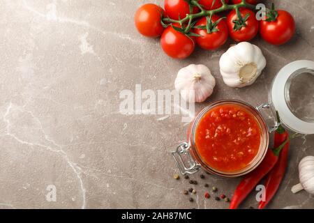 La sauce Chili dans un bocal en verre et d'ingrédients sur fond gris, de l'espace pour le texte Banque D'Images