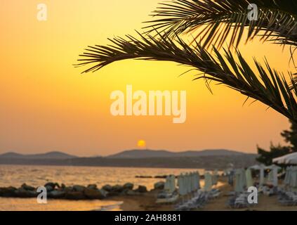 Chaises longues et parasol sur la plage au coucher du soleil par la mer. Locations et voyage concept. Banque D'Images